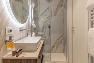 Un baño moderno con una bañera independiente grande, una ducha con mampara de vidrio y un revestimiento de mármol.