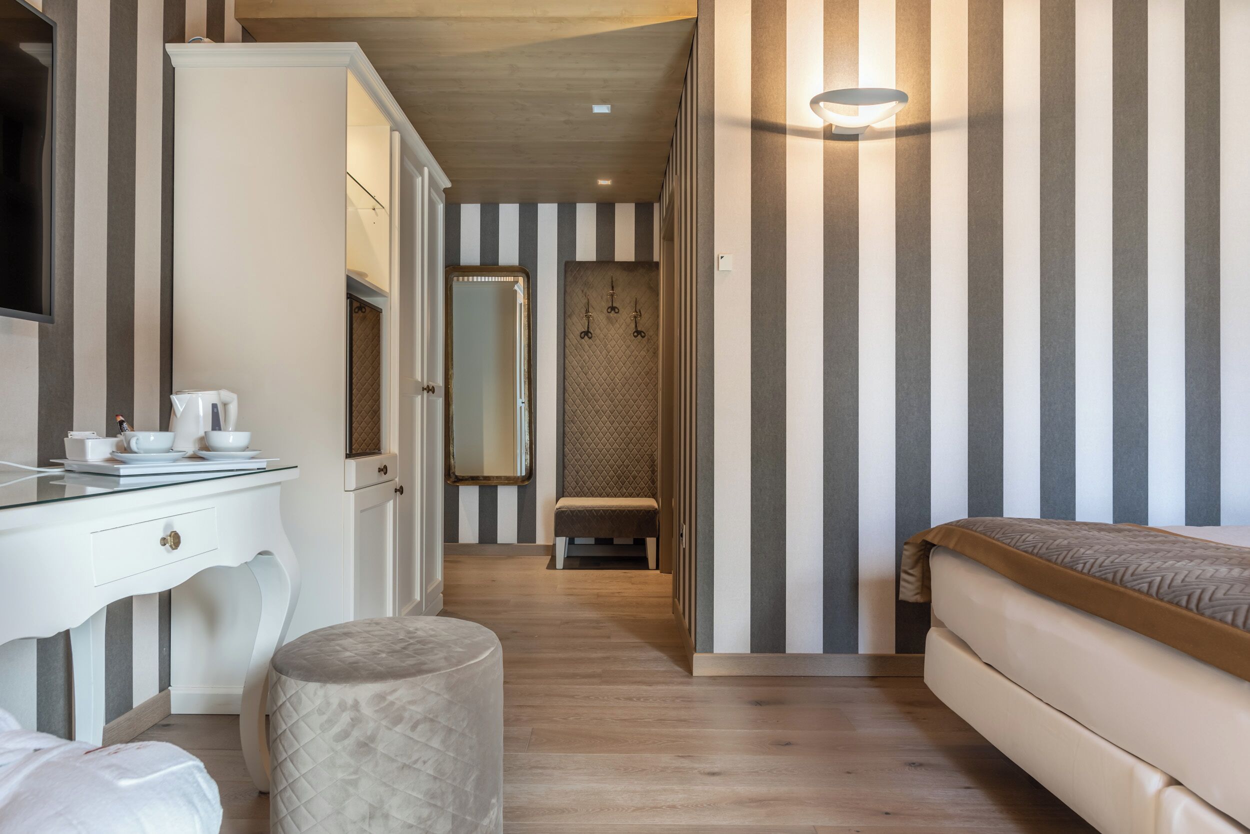 Habitación de hotel con pared a rayas, una cama, una tocador con espejo y un taburete pequeño.