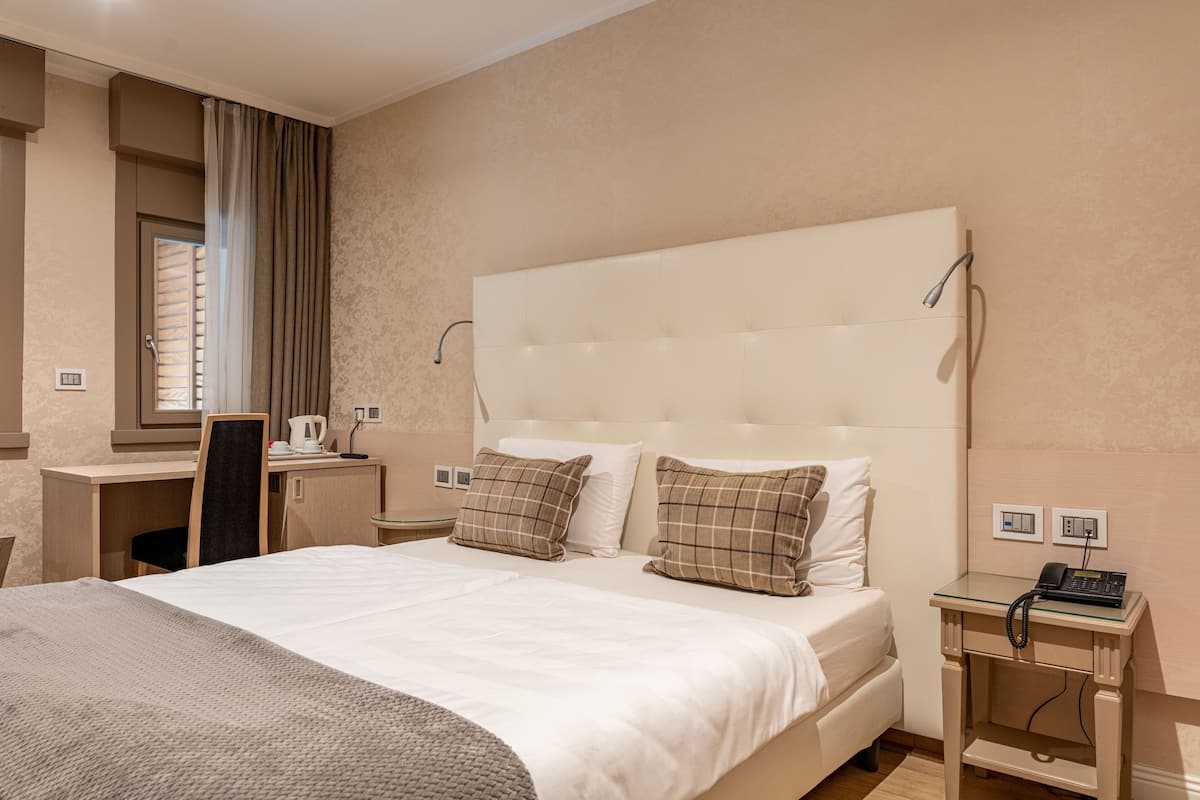 Ein Hotelzimmer mit einem großen Bett, einem Schreibtisch, einem Stuhl und einem kleinen Tisch mit einem Telefon.