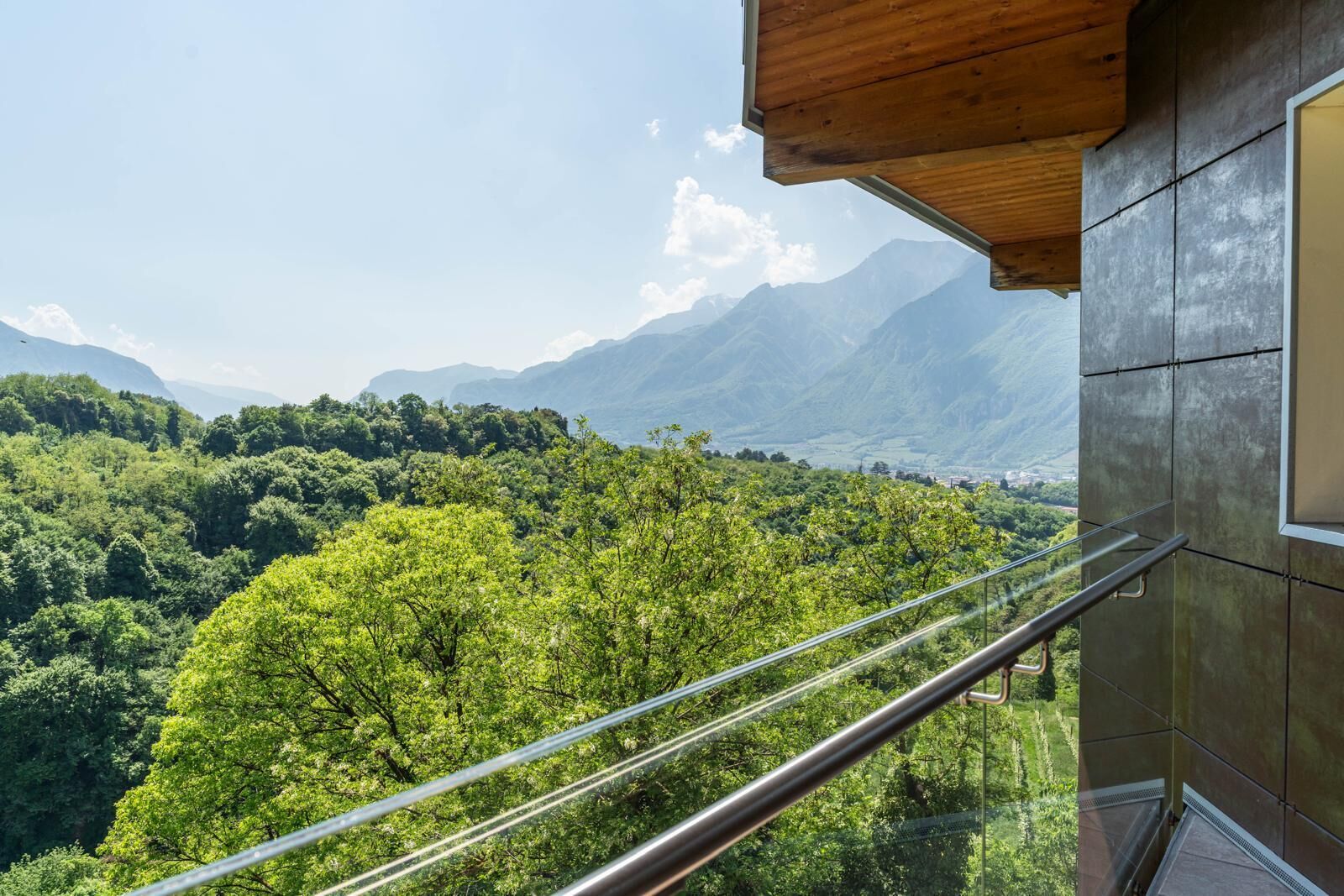 Ein Balkon mit Metallgeländer, der einen üppigen, grünen Wald und ferne Berge überblickt.