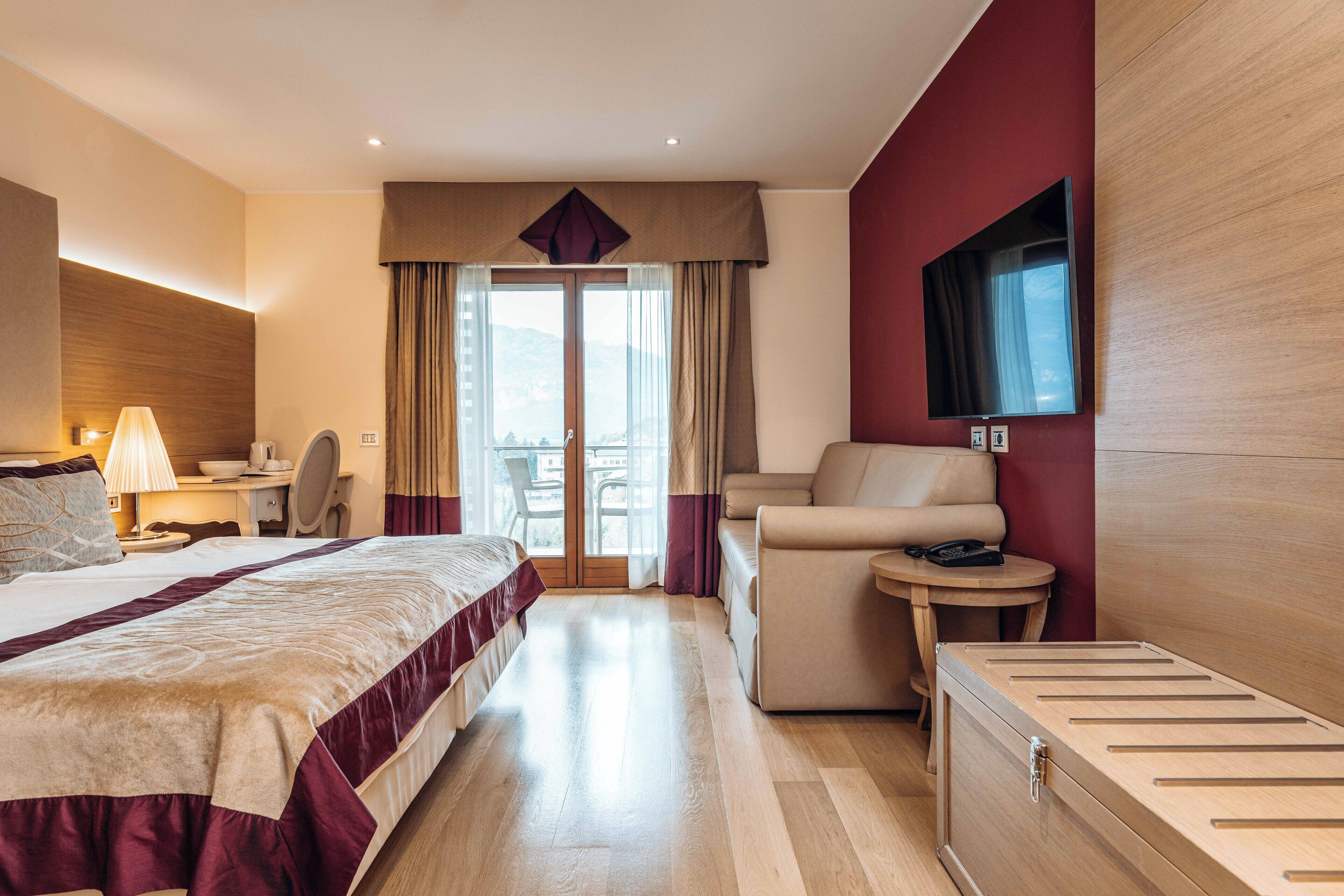 A hotel room with a bed, a sofa, a desk, a chair, and a TV.