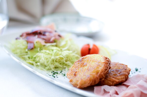 Un plato con vegetales desmenuzados, un tomate y dos hamburguesas doradas sobre una vajilla blanca.