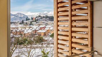 A room with a large window overlooking a snowy village and mountains.