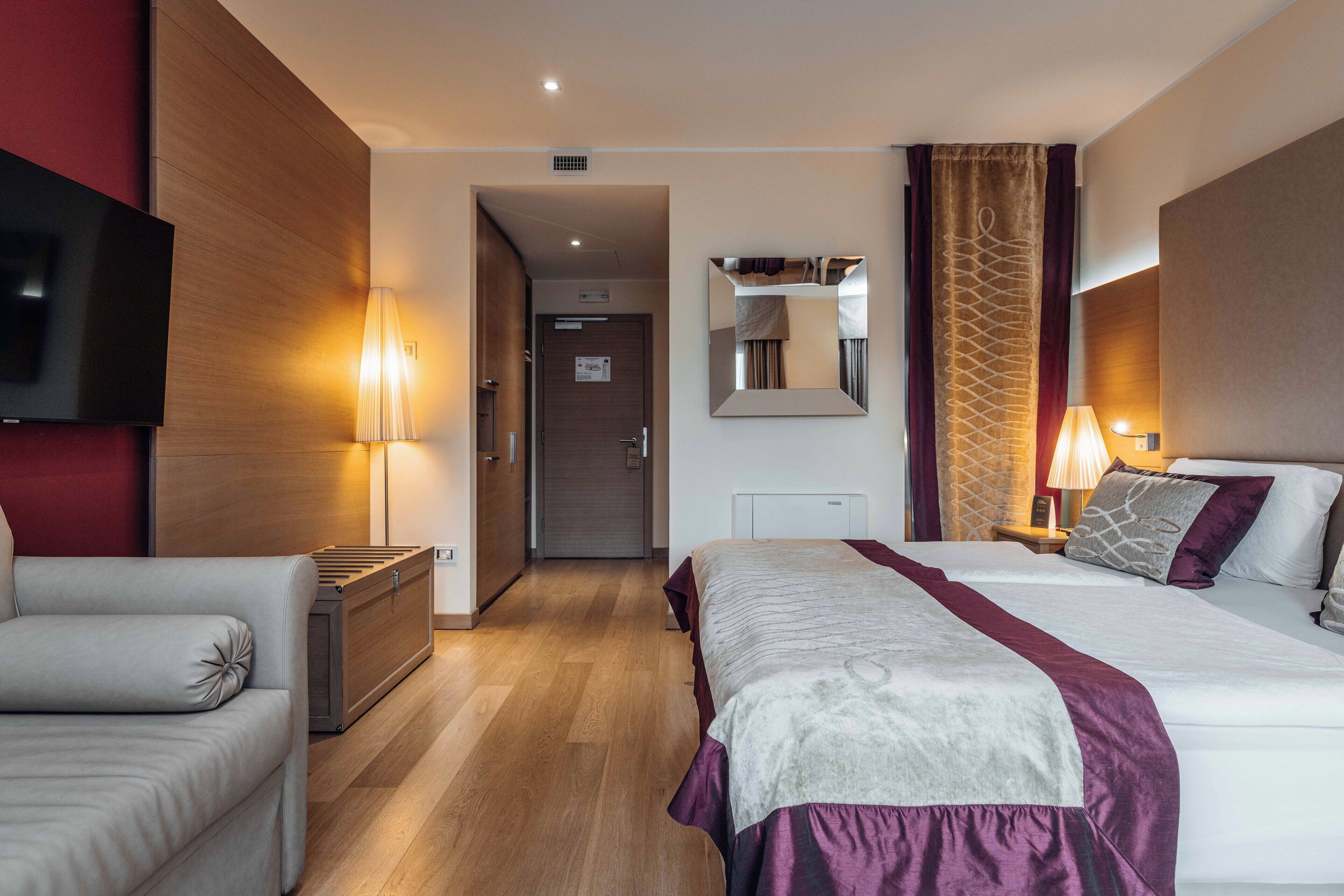 A hotel room with two beds, a TV, a desk, a lamp, and a mirror.