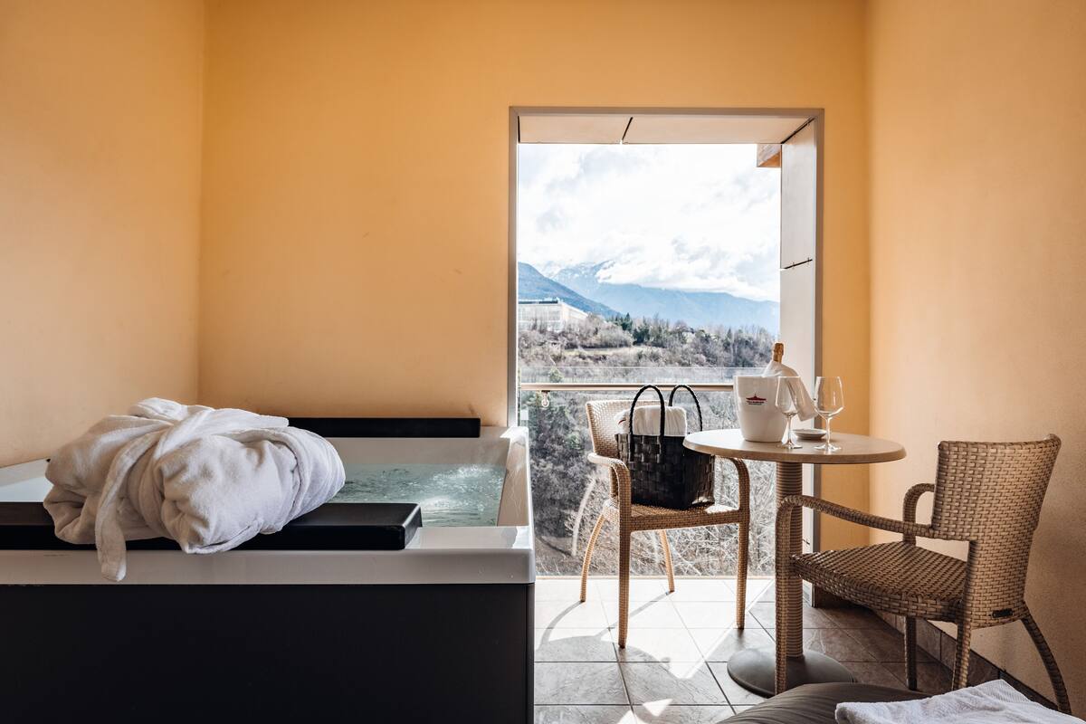 Ein Zimmer mit einer Badewanne, einem Tisch mit Korb und Glas sowie einem Sessel.