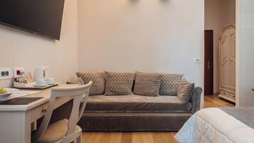Una habitación funcional con sofá, escritorio y silla, cama, armario y televisor de pantalla plana en la pared.