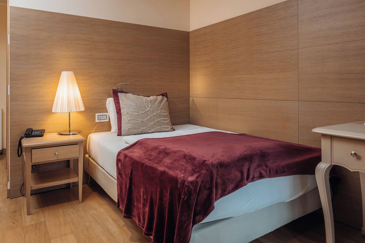 Ein Hotelzimmer mit Bett, Nachttischlampe, Beistelltisch und einer Wandverkleidung aus Holz.