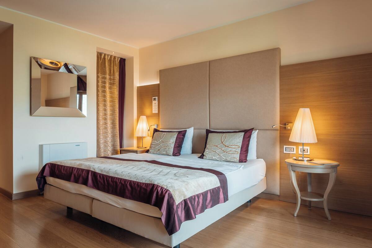 Ein Hotelzimmer mit einem großen Bett, zwei Nachttischen mit Lampen, einem Spiegel und einem Holzkopfende.