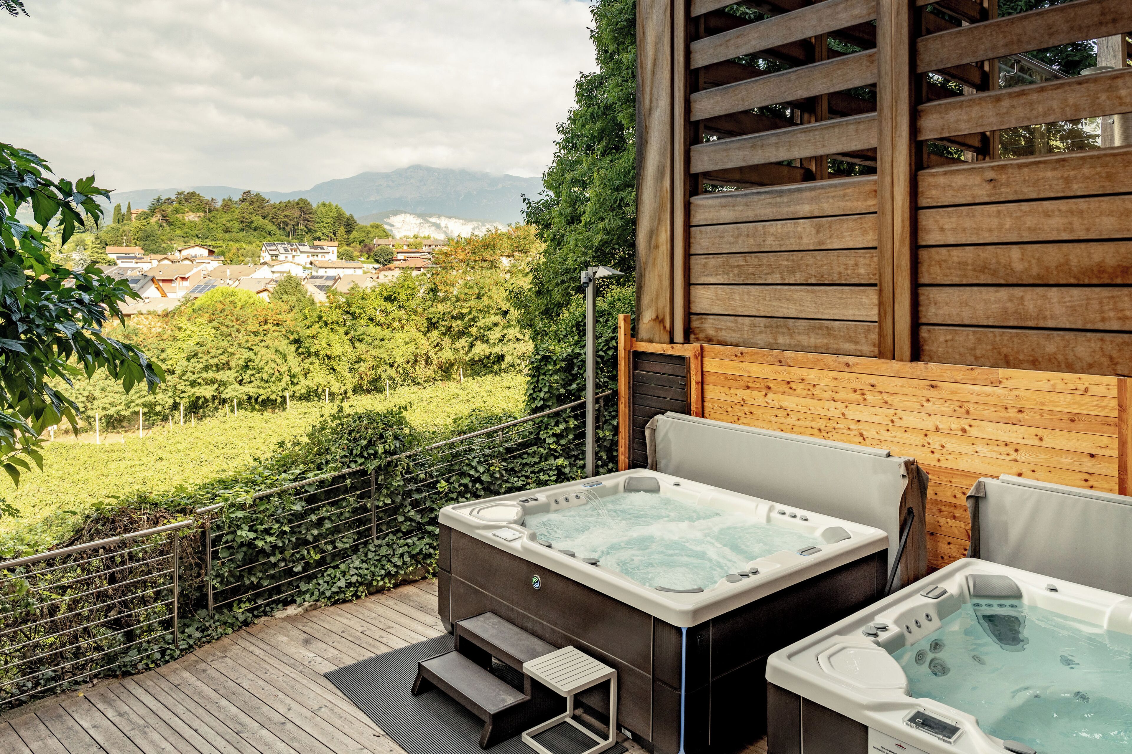Eine Holzterrasse mit zwei Whirlpools und Blick auf eine üppige grüne Landschaft sowie entfernte Berge.