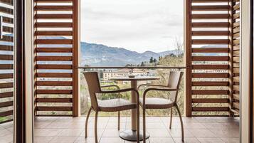 A balcony with wicker chairs and a table, overlooking a mountainous landscape.