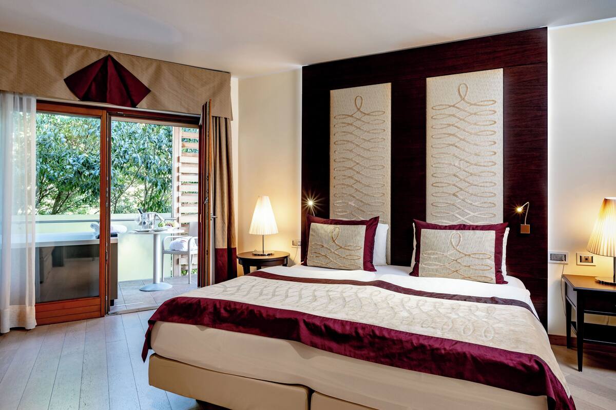 Ein Hotelzimmer mit einem großen Bett, einem Balkon und Blick auf Bäume.
