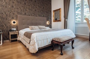 A bedroom with a large bed, bedside tables, a nightstand, a bench, a mirror, and a window with curtains.