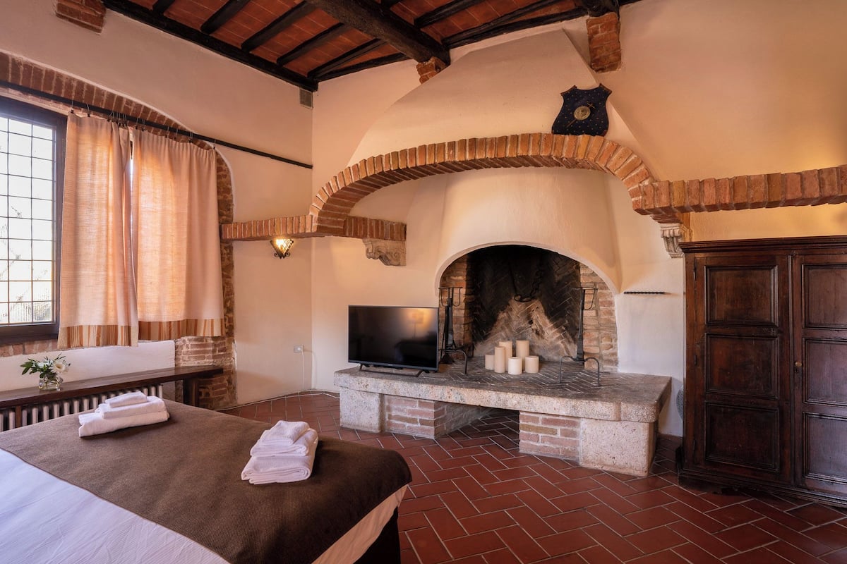 A room with a fireplace, a bed with towels, a television, and a wooden cabinet.