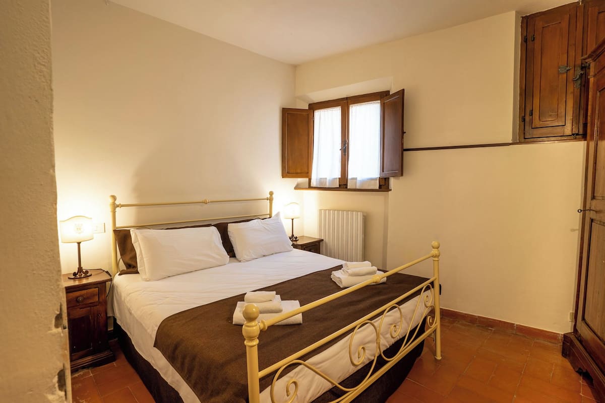 A bedroom with a bed, bedside lamps, a radiator, and a wooden wardrobe.