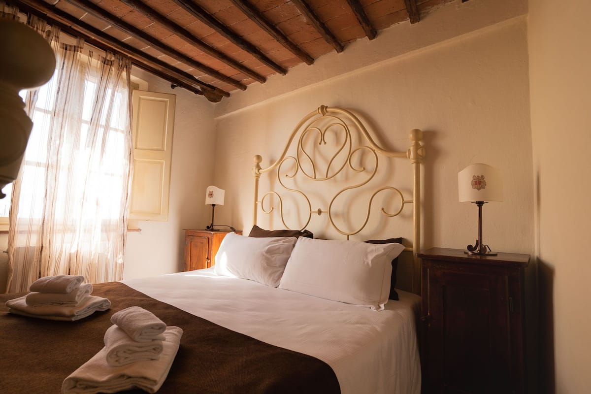 A hotel room with a bed, two bedside tables, a window with curtains, and a wooden ceiling.