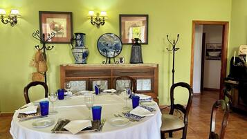 A dining room with a round table set for four, surrounded by chairs. There are wall-mounted light fixtures and framed pictures above the table.