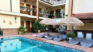 A pool area with a tiled floor, lounge chairs, and umbrellas.