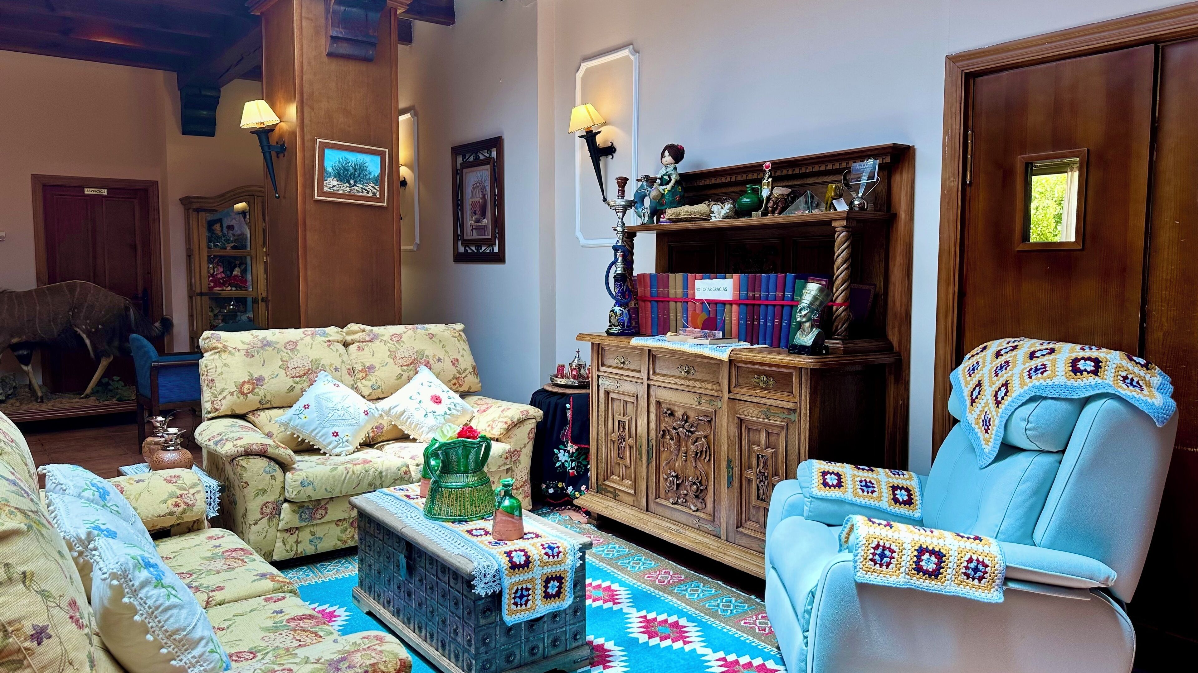Una sala de estar acogedora con muebles de estampado floral, un aparador de madera con libros y una cabeza de animal montada.