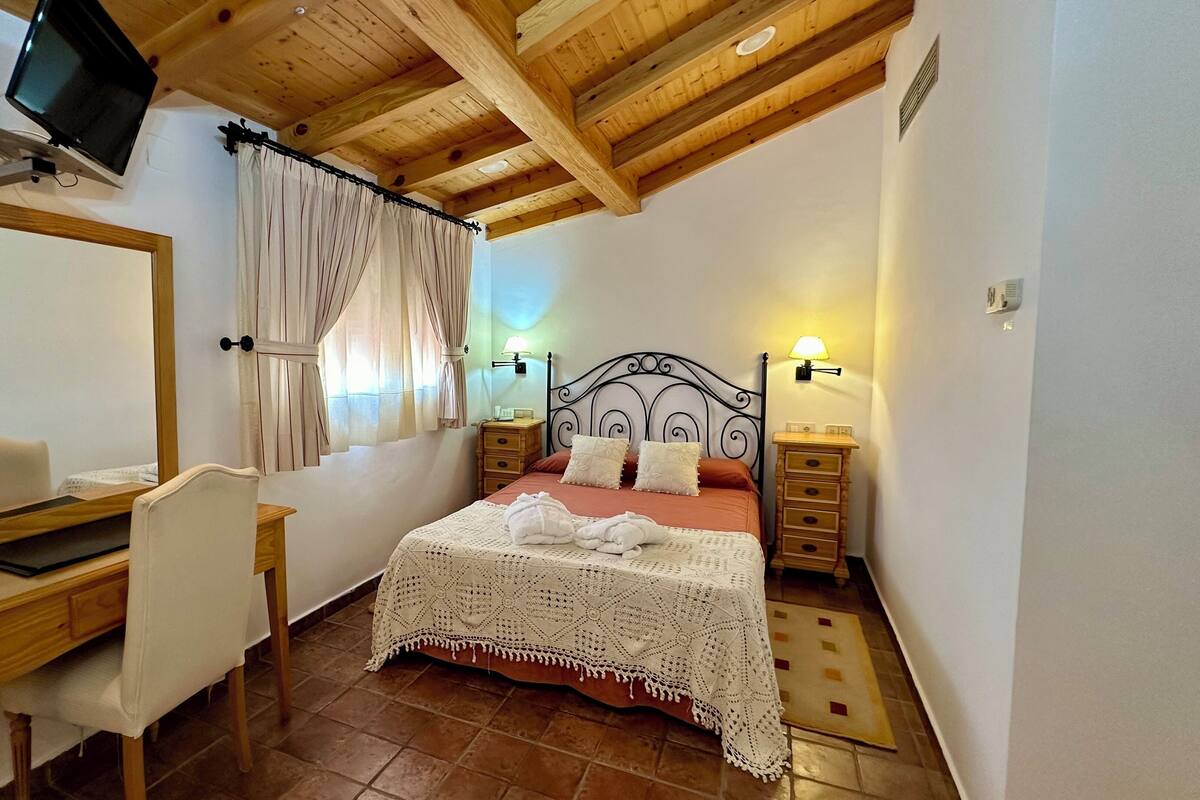 A bedroom with a bed, bedside tables, a desk, a chair, a TV, and a window with curtains.