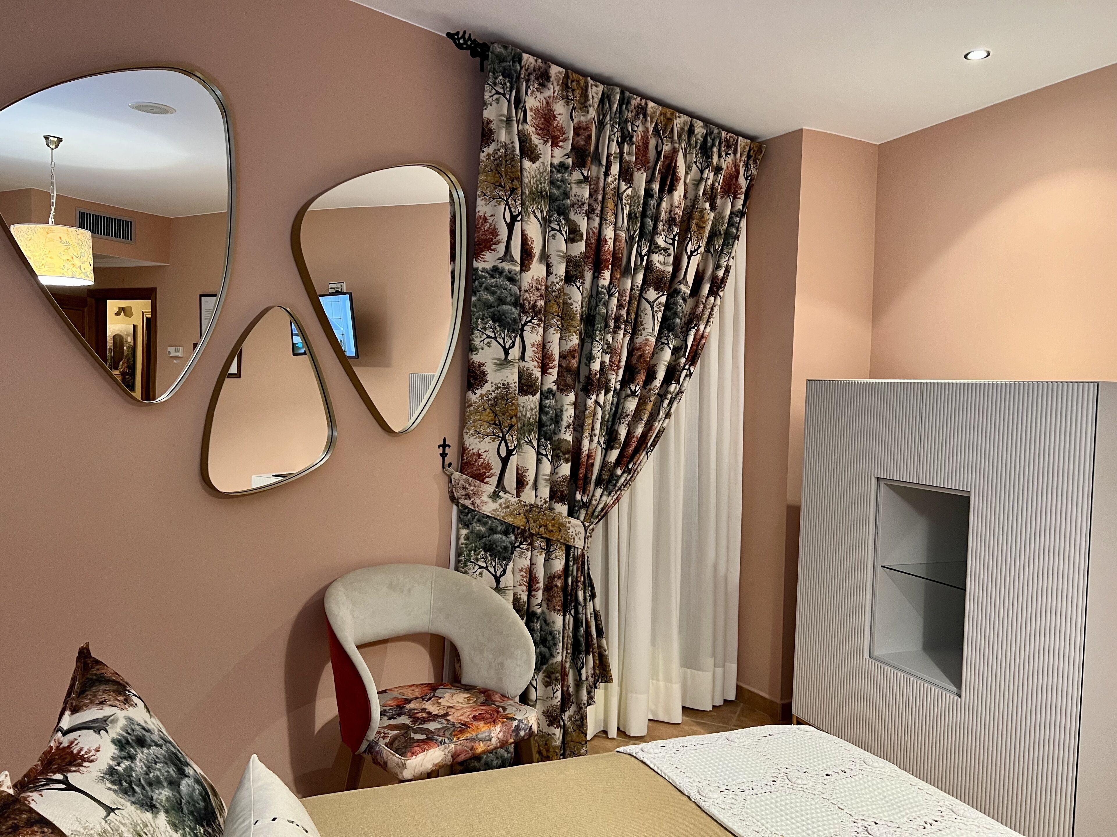 Una sala moderna con un sofá, una butaca, un espejo grande y una cortina estampada.
