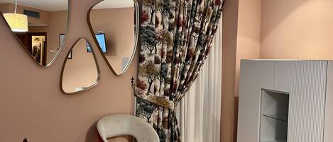Una sala moderna con un sofá, una butaca, un espejo grande y una cortina estampada.
