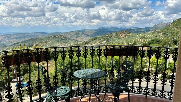 A balcony with ornate metal railings, a small table, and a chair.