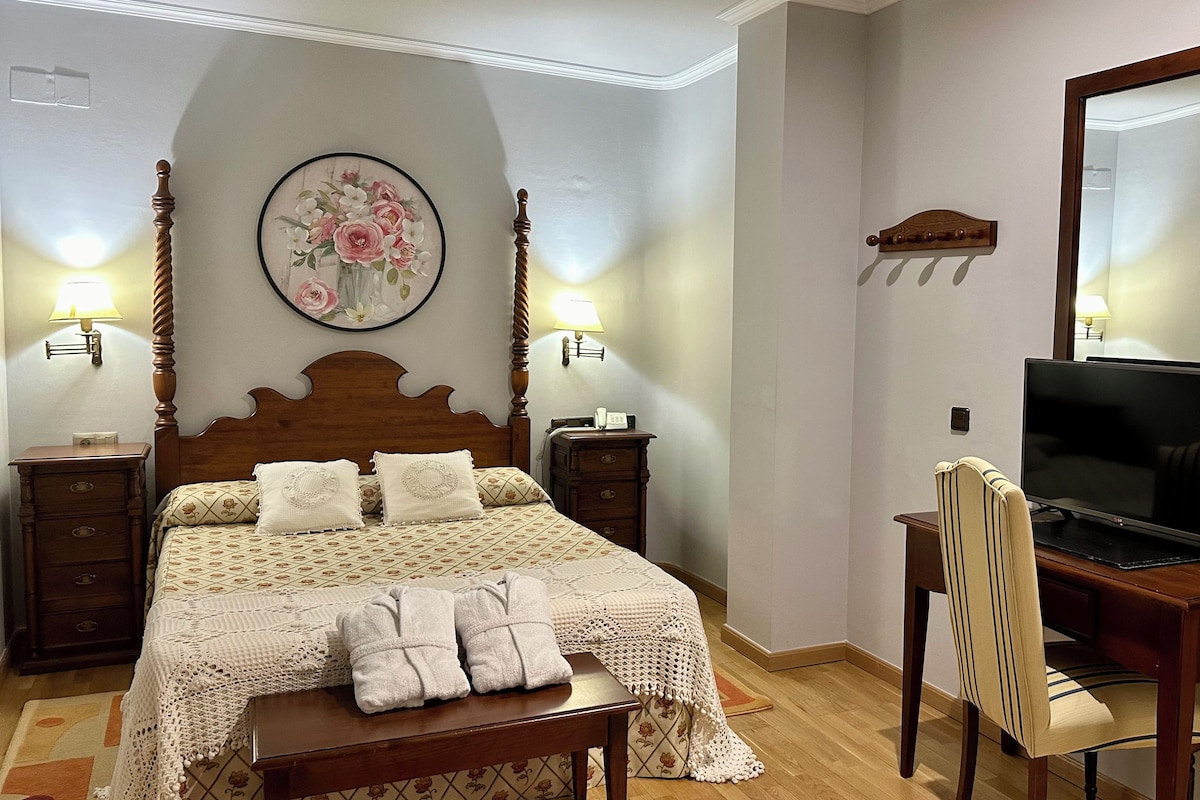 A neatly arranged bedroom with a bed, bedside lamps, a television, and a chair.