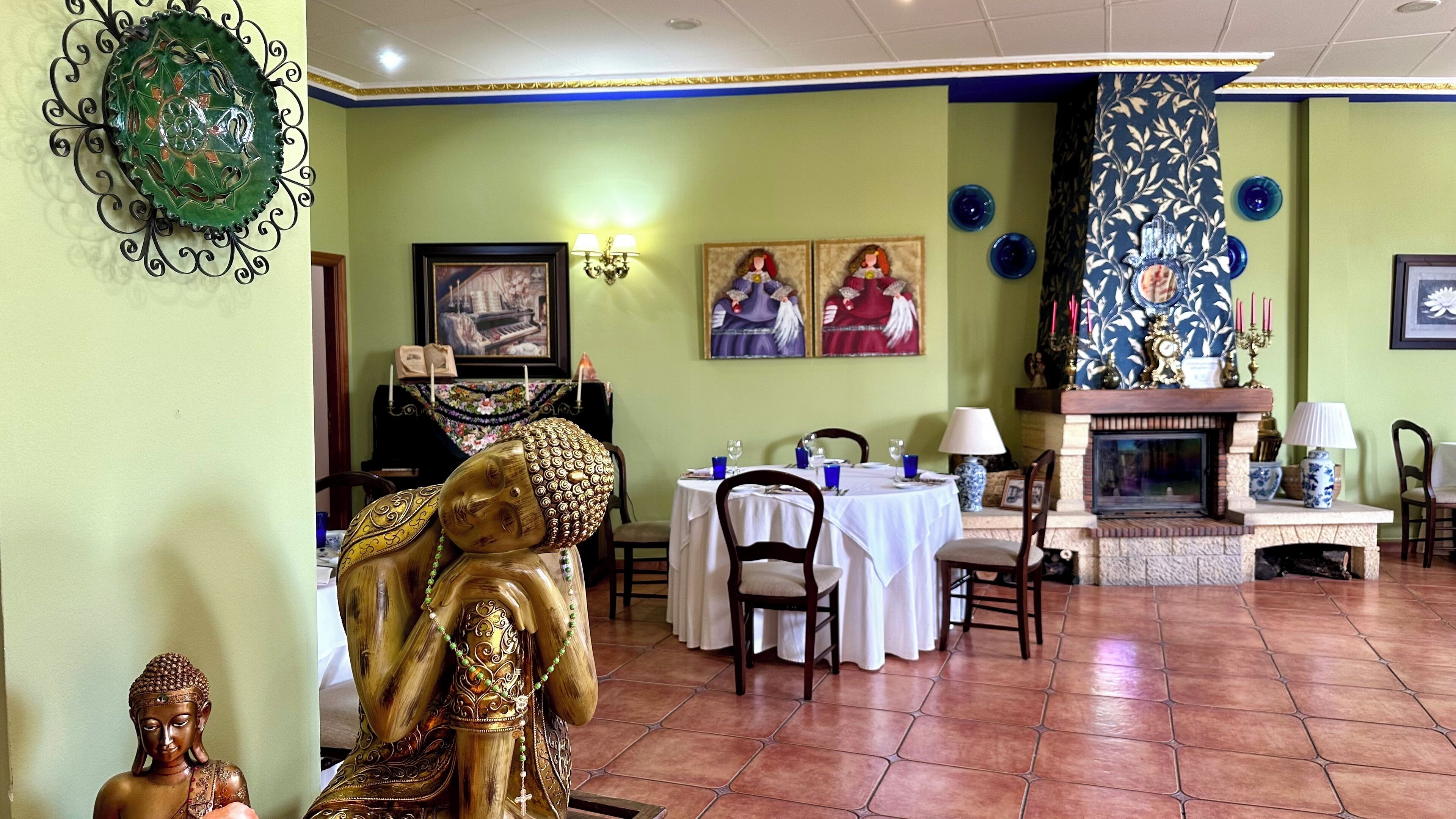 A dining area with a table set for two, a fireplace, and a Buddha statue.