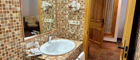 Un baño con pared de azulejos, un lavamanos, un espejo y una puerta que da a otra habitación.