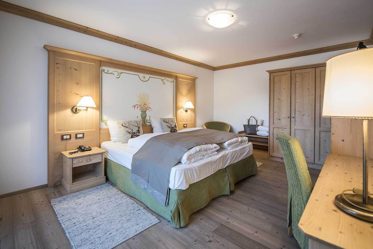 A bedroom with a bed, bedside lamps, a nightstand, a chair, a desk, and a wardrobe.