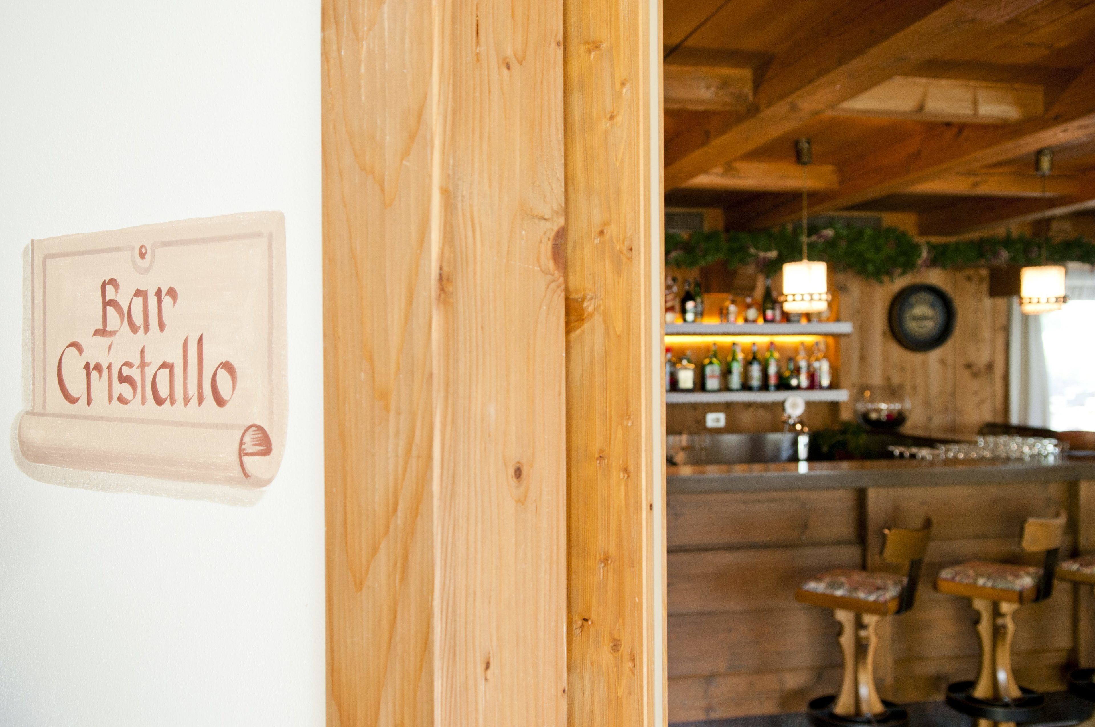 A wooden interior with a bar named 'Bar Cristallo' and a bar counter with bottles and glasses.