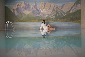 A person sitting on a pool edge with a mountainous landscape in the background. - Hotel Cristallo (Dobbiaco)