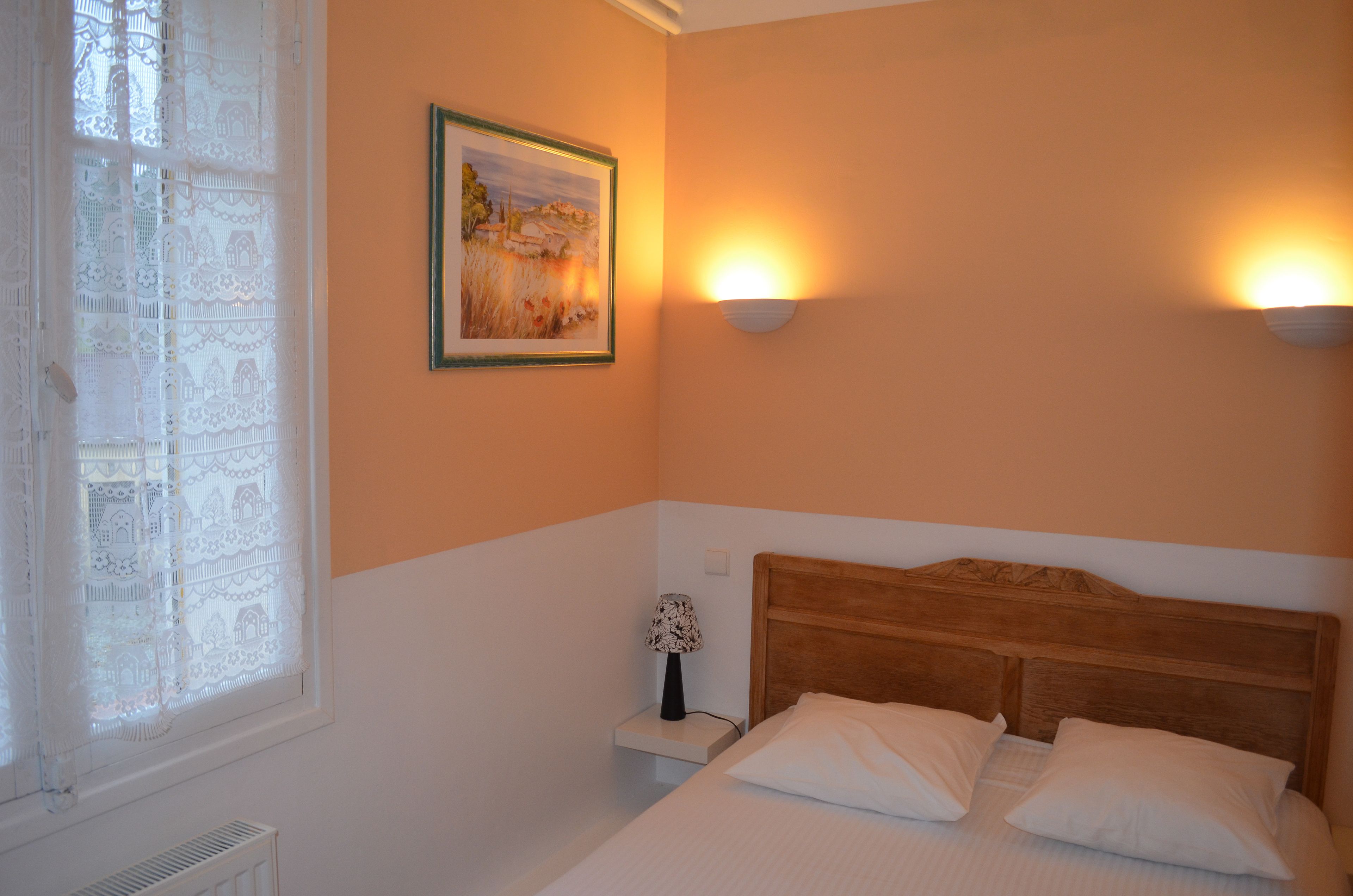 A bedroom with a wooden headboard, a bed with white bedding, a nightstand with a lamp, and a framed picture on the wall.
