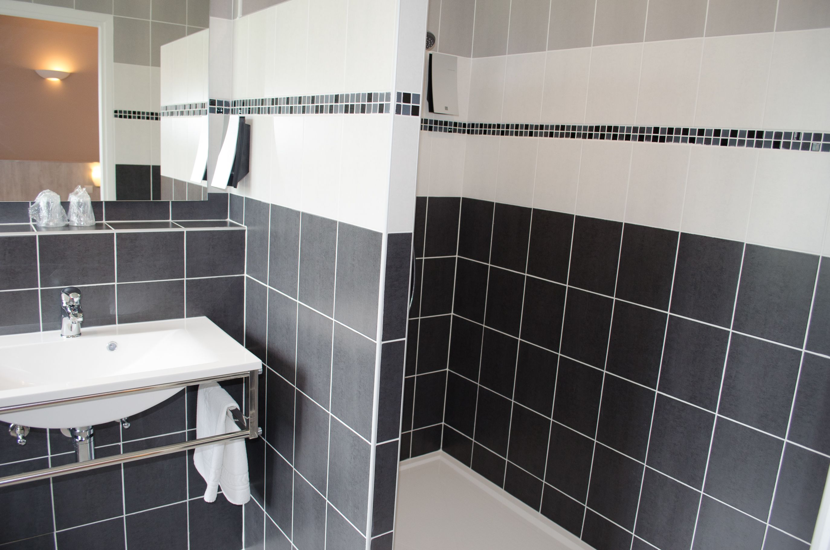A bathroom with a white sink, black and white tiled walls, and a mirror above the sink.