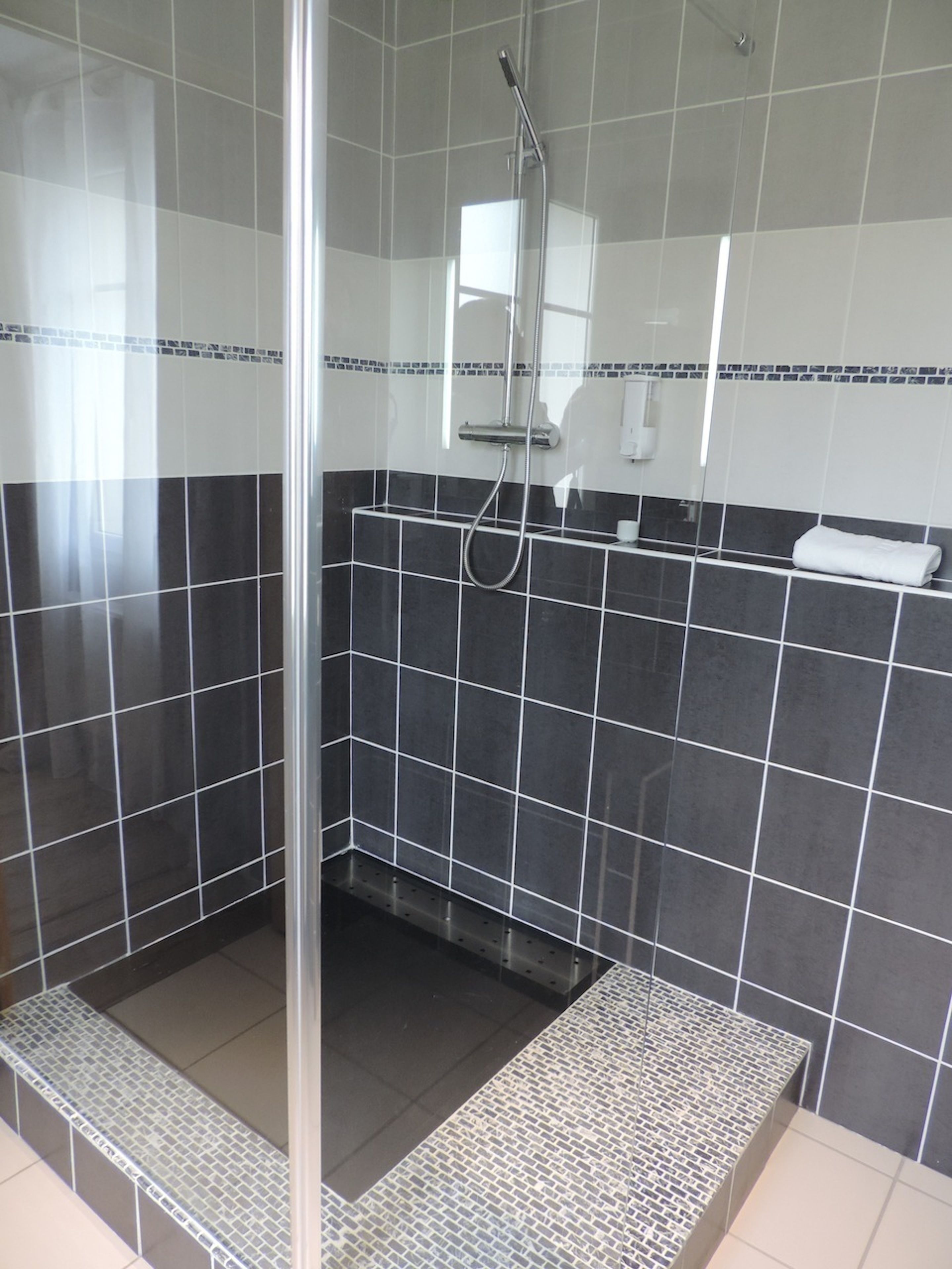 Ein modernes Duschbad mit Glastür, gefliesten Wänden und einer Metallbank.