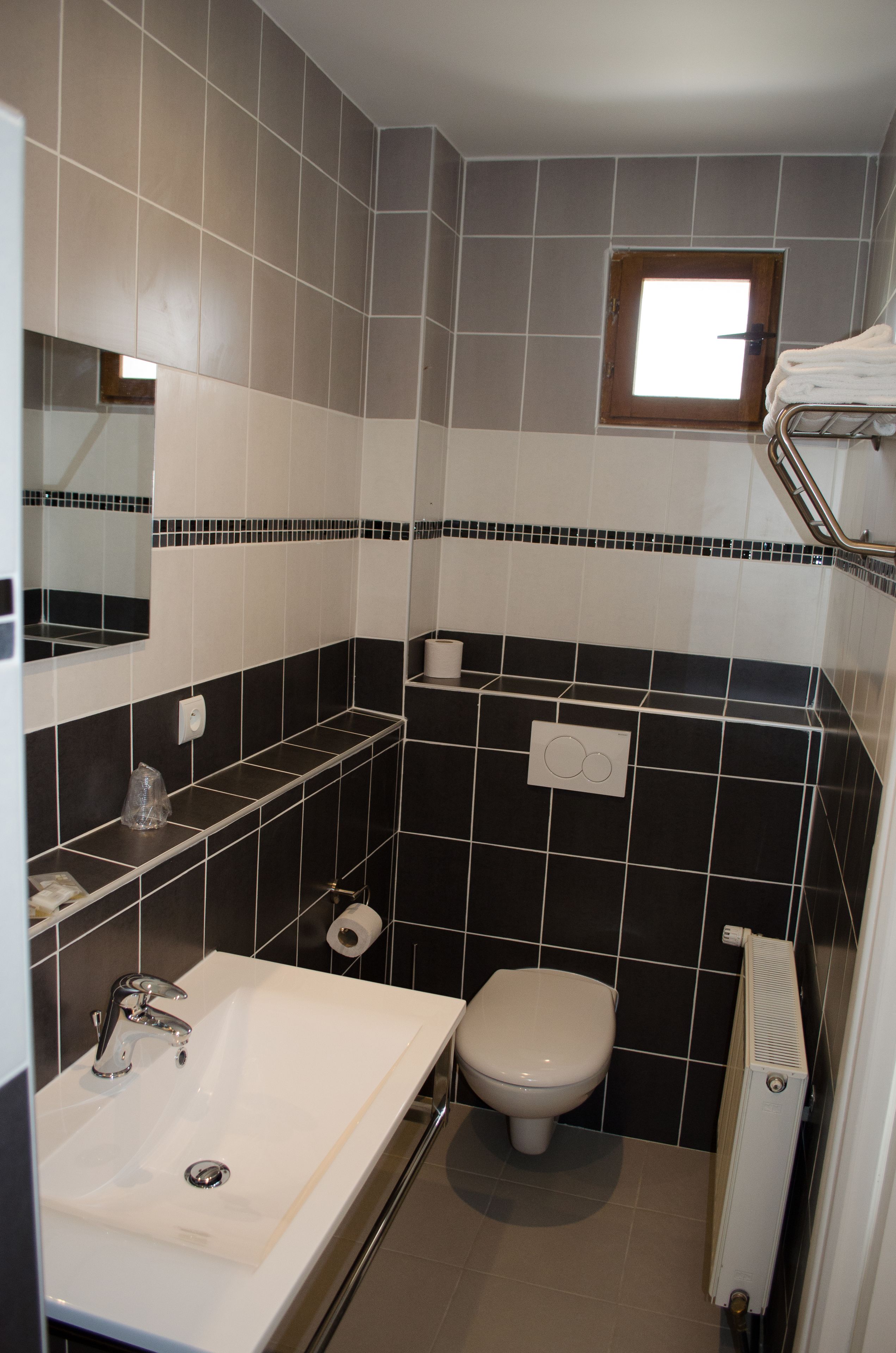 Un baño con un lavamanos blanco, un inodoro y un ventanal pequeño.