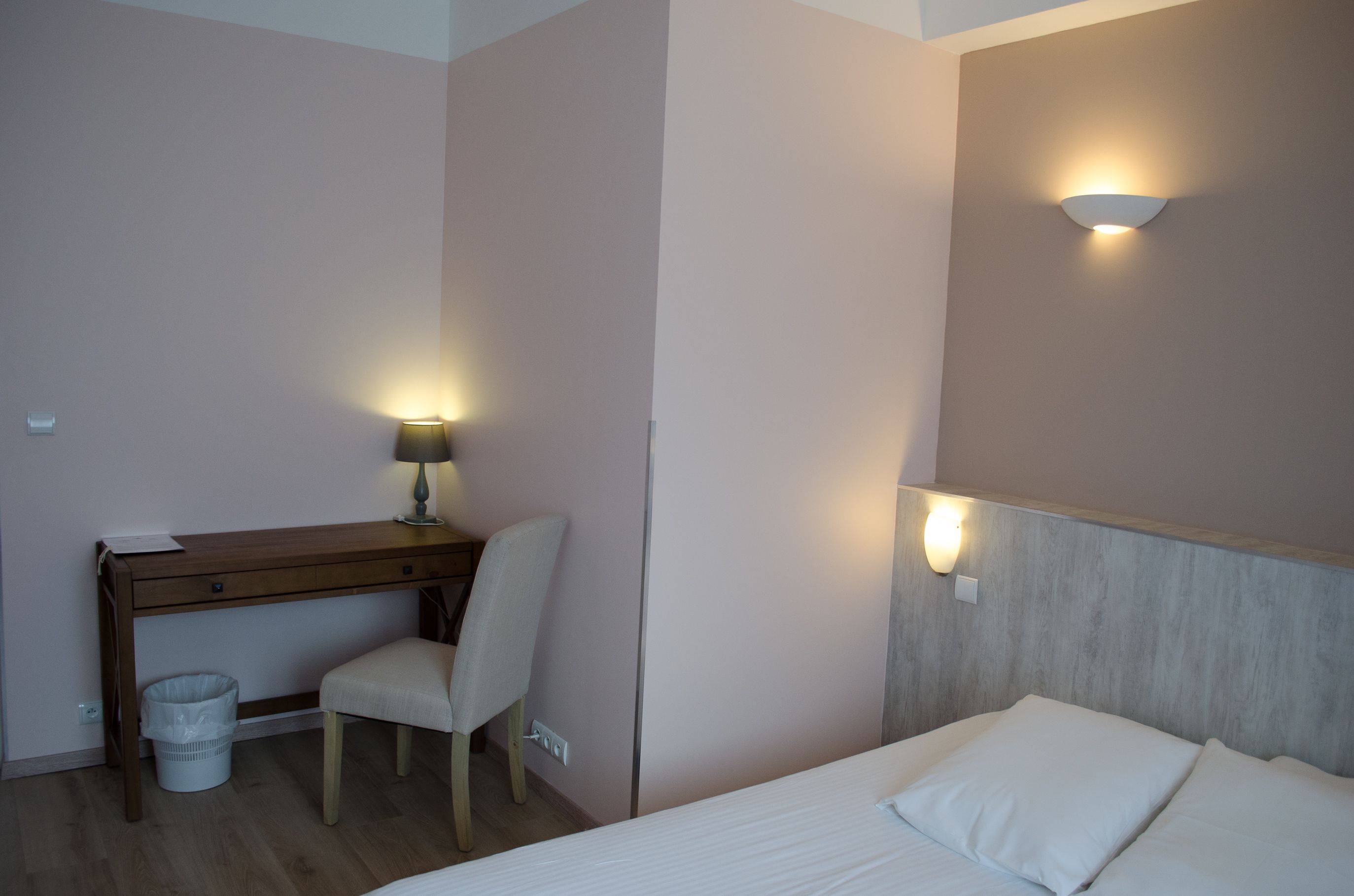 Habitación de hotel con cama, escritorio, silla, lámpara e iluminación en la pared.