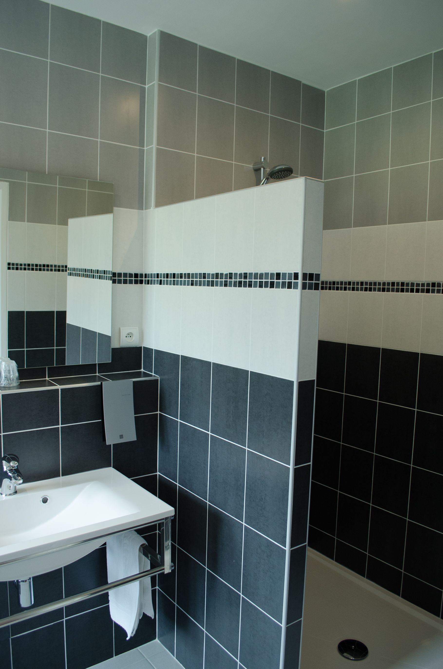 A bathroom with a white sink, black and white tiled walls, a mirror, and a shower area.