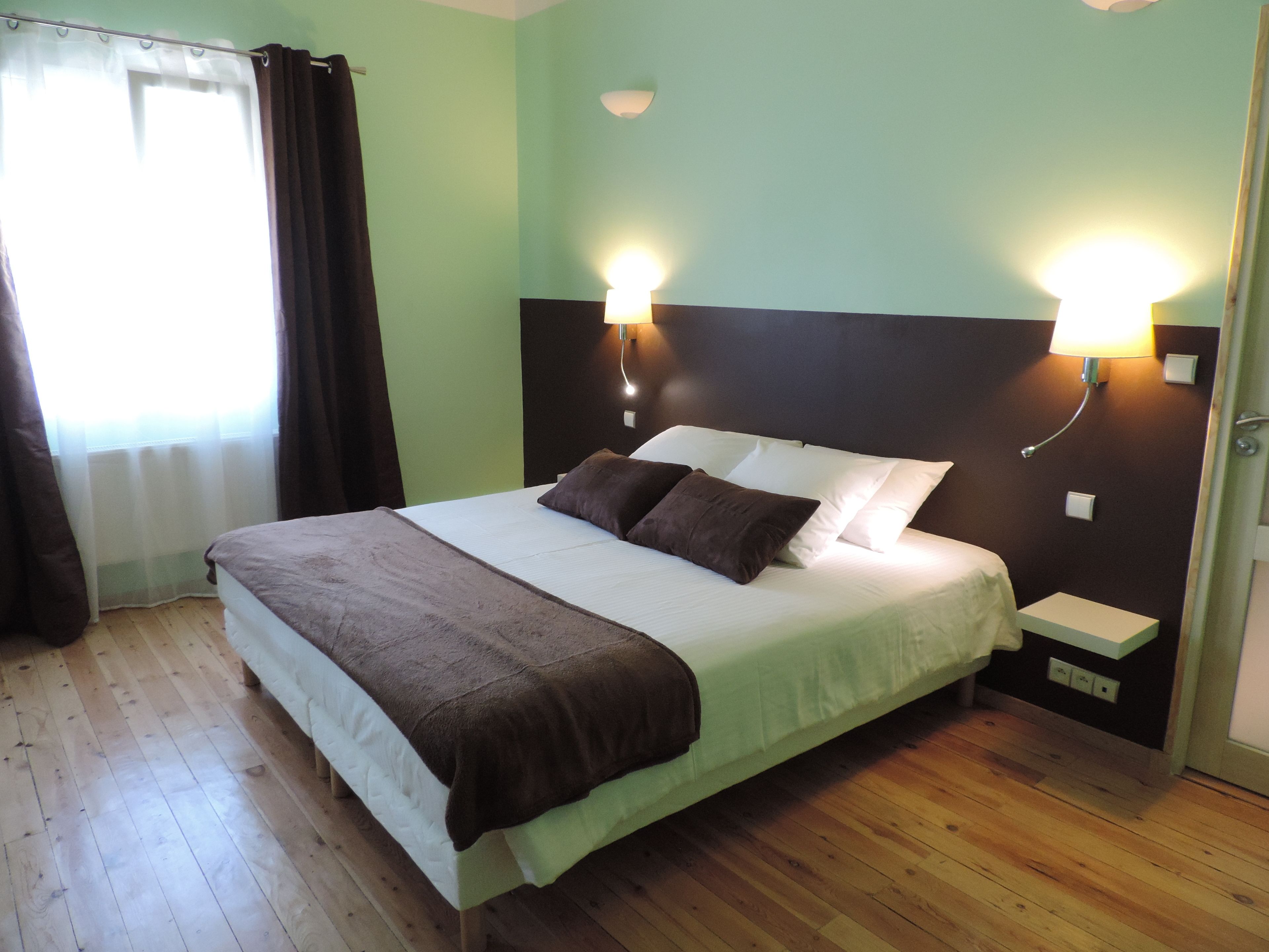 Una cama bien hecha con una manta y almohadas marrones, una mesita de noche con una lámpara y un suelo de madera.