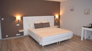 Een slaapkamer met een groot bed, twee bedlampen, een klein tafeltje met een waterkoker en een muur met twee bloemschilderijen.