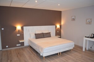 Quarto com uma cama grande, duas luminárias de cabeceira, uma mesinha com chaleira e um painel com dois quadros de flores.