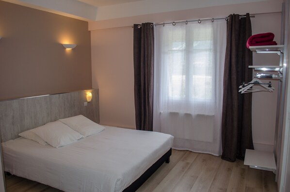 A bedroom with a bed, a wall-mounted light, a window with curtains, and a towel rack.