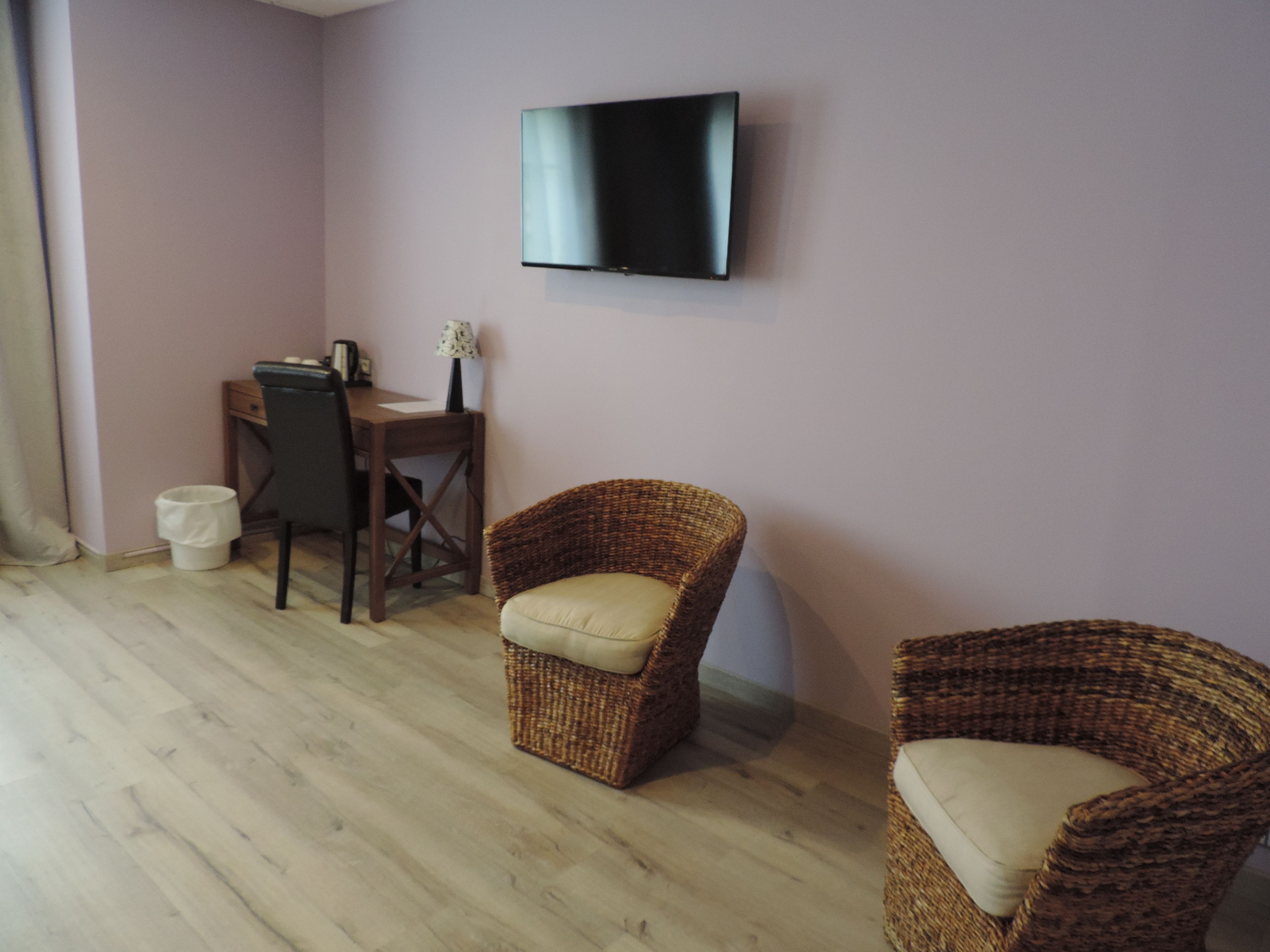 Una habitación con una televisión de pantalla plana montada en la pared, un escritorio de madera con una silla, y dos sillones de mimbre.