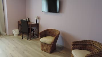 Una habitación con una televisión de pantalla plana montada en la pared, un escritorio de madera con una silla, y dos sillones de mimbre.