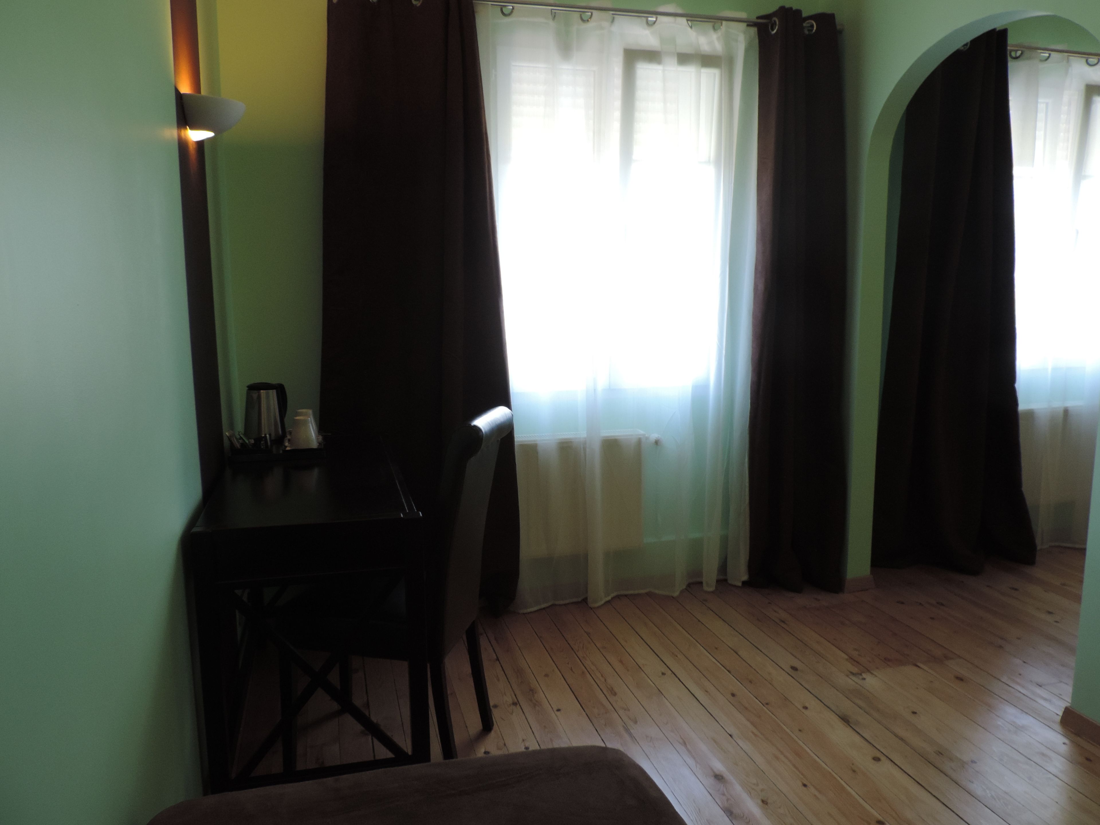 A room with a wooden floor, a desk with a chair, a radiator, and a window with curtains.