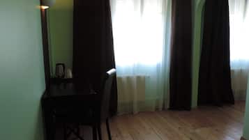 A room with a wooden floor, a desk with a chair, a radiator, and a window with curtains.