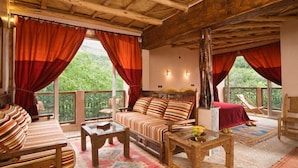 A cozy room with a wooden ceiling, a sofa, a coffee table, and a balcony with red curtains.