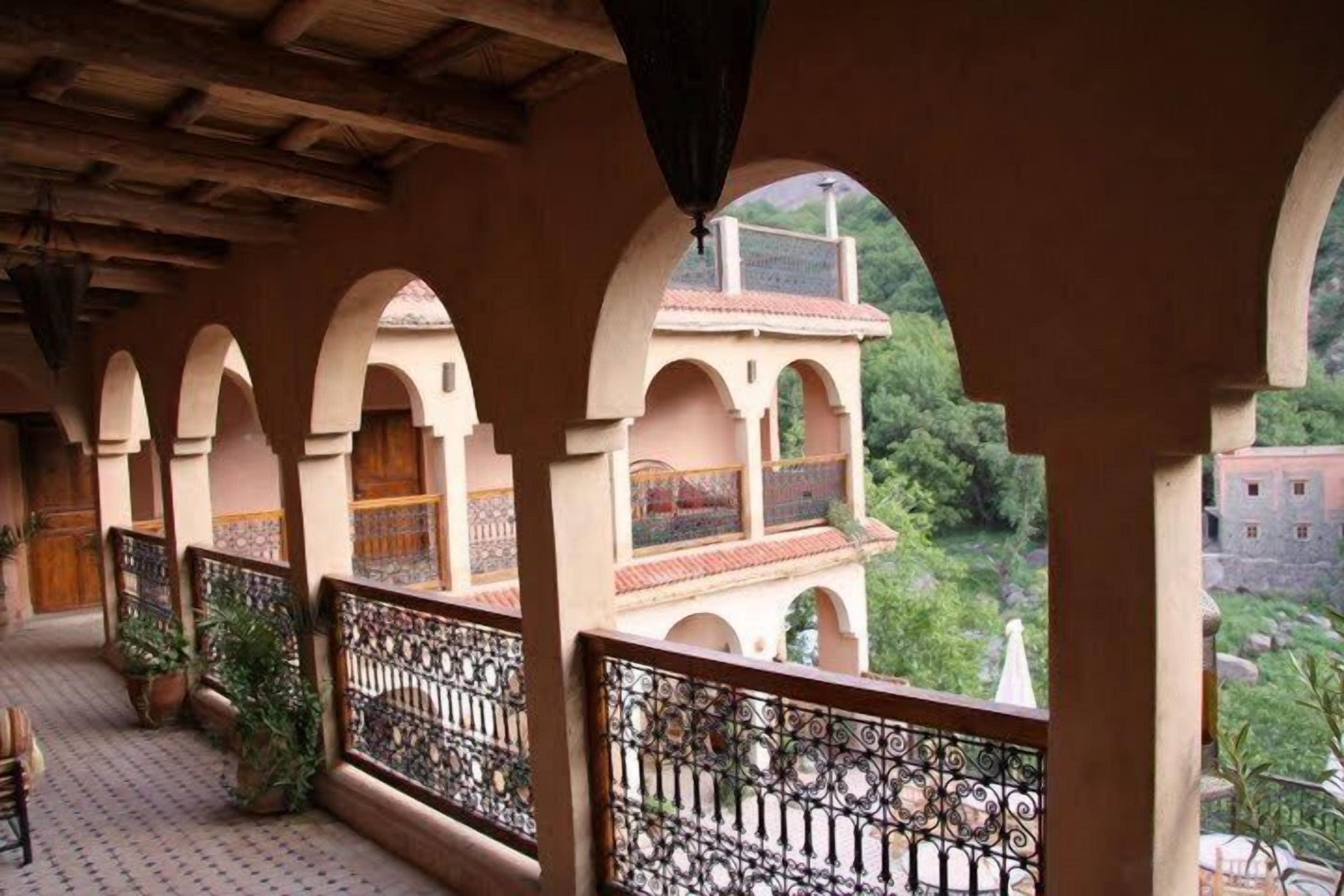 A covered balcony with arches, a patterned floor, and a view of greenery and buildings in the background.