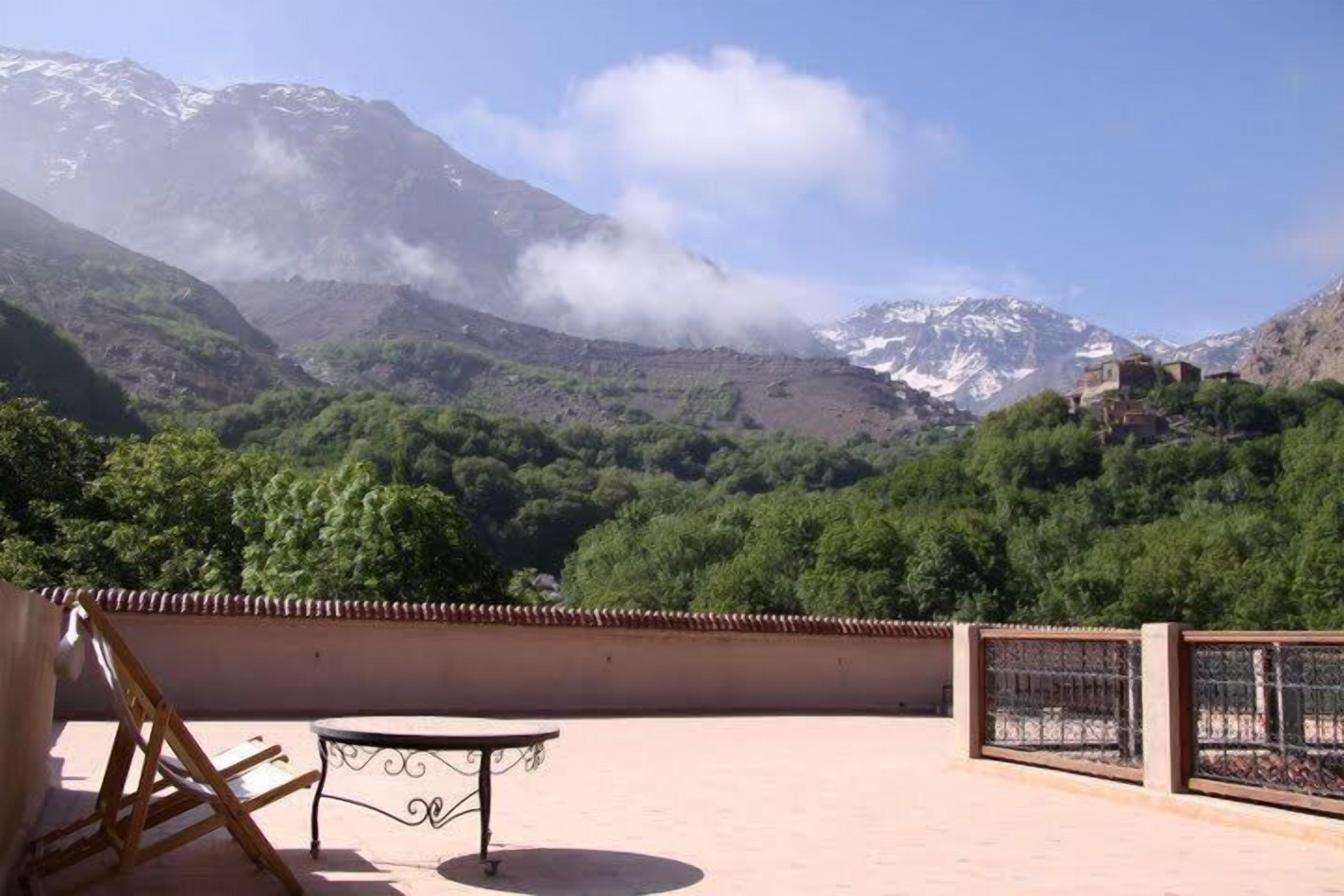 Une terrasse avec une table et des chaises, offrant une vue sur un paysage montagneux verdoyant, avec un bâtiment perché sur une colline.