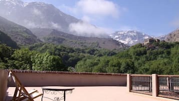 Una terraza con mesa y sillas, con vistas a un paisaje montañoso con vegetación y un edificio en una colina.